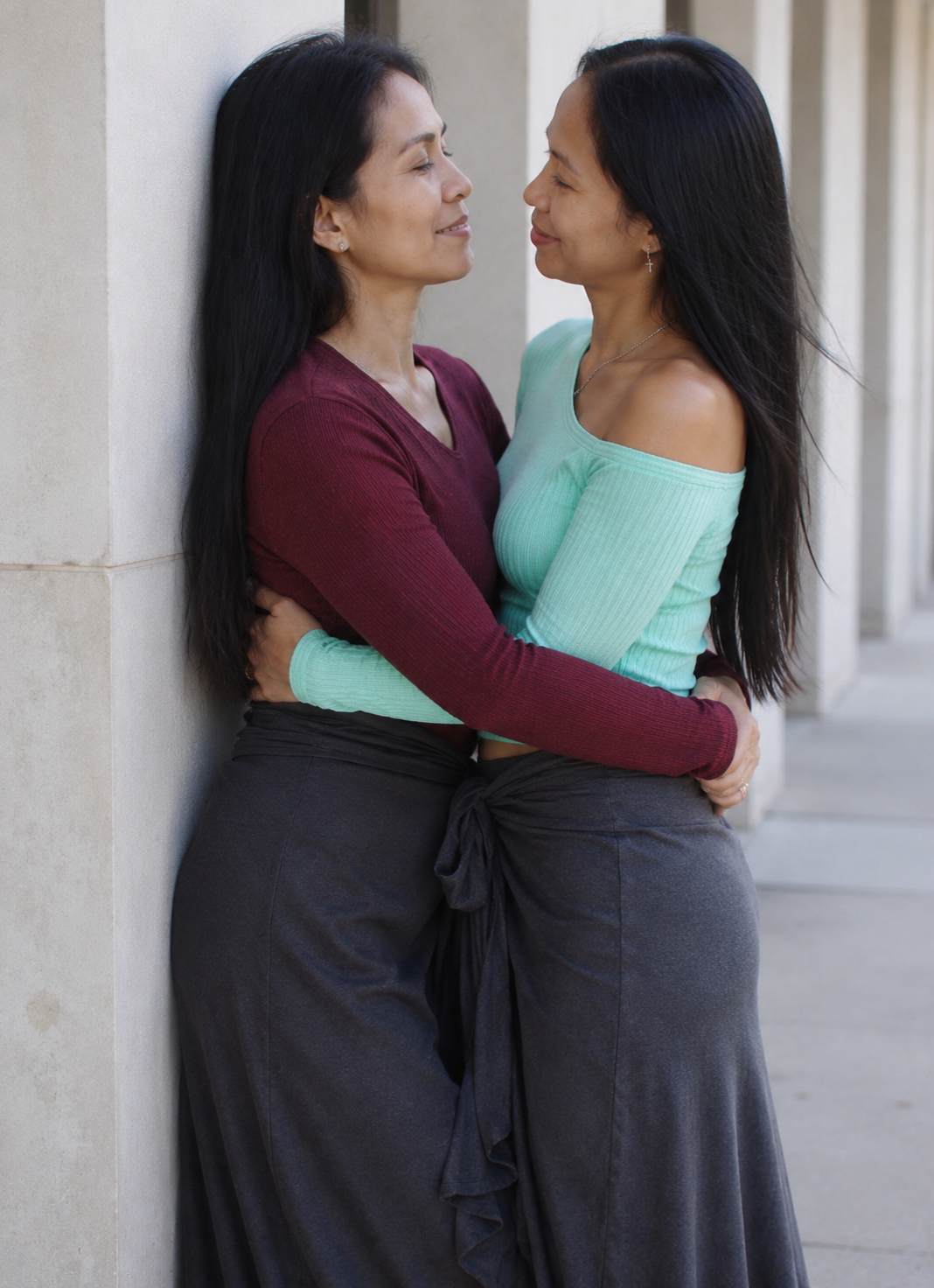Two women stand face-to-face in the corridor — hands clasped, the moment of meeting at the threshold